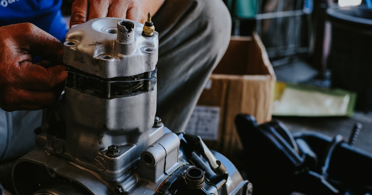 Close-up of a man’s hands working on fixing a two-stroke cylinder head engine inside a mechanic workshop.